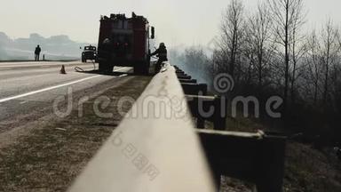 消防队员从对面的消防车上解开消防水带，扑灭森林中的火灾和干草